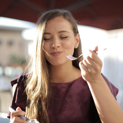 A woman with her eyes closed smiling while holding a fork and enjoying a meal.