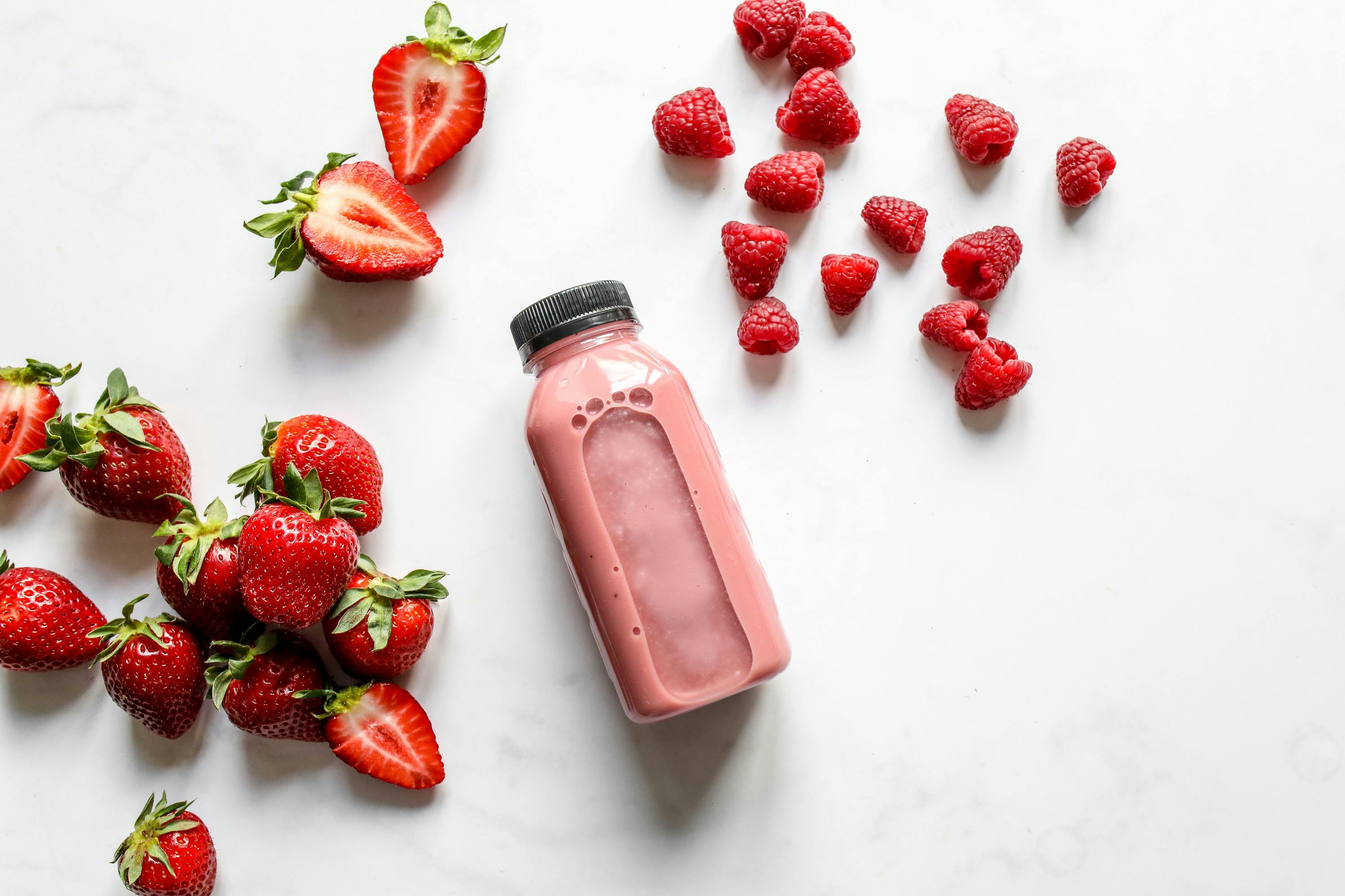 Pink smoothie bottle with strawberries and raspberries on white background.