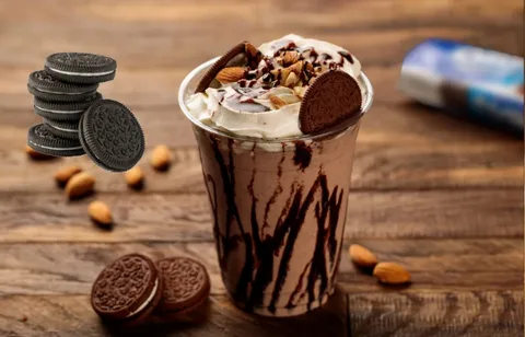 Chocolate milkshake topped with whipped cream, almonds, and a cookie on a rustic wooden surface.